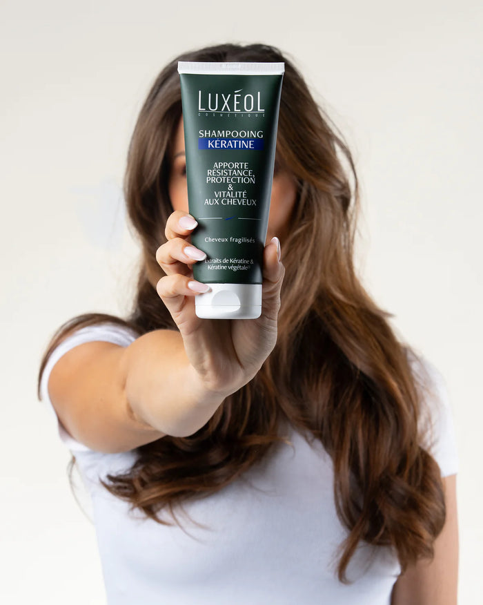 Person holding a Luxeol shampoo bottle with a plain background