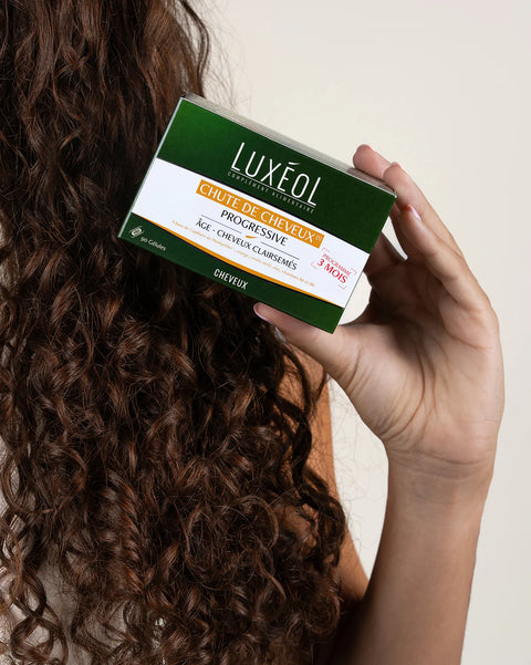 Person holding a Luxeol hair care product box with curly hair.