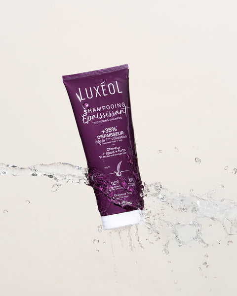 Violets Luxéol šampūna tūbiņa uz bēša fona ar ūdens pilieniem