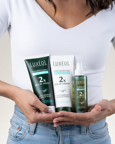 Persona, kas tur Luxéol matu kopšanas produktus, tostarp šampūnu, kondicionieri un izsmidzināmu miglu.